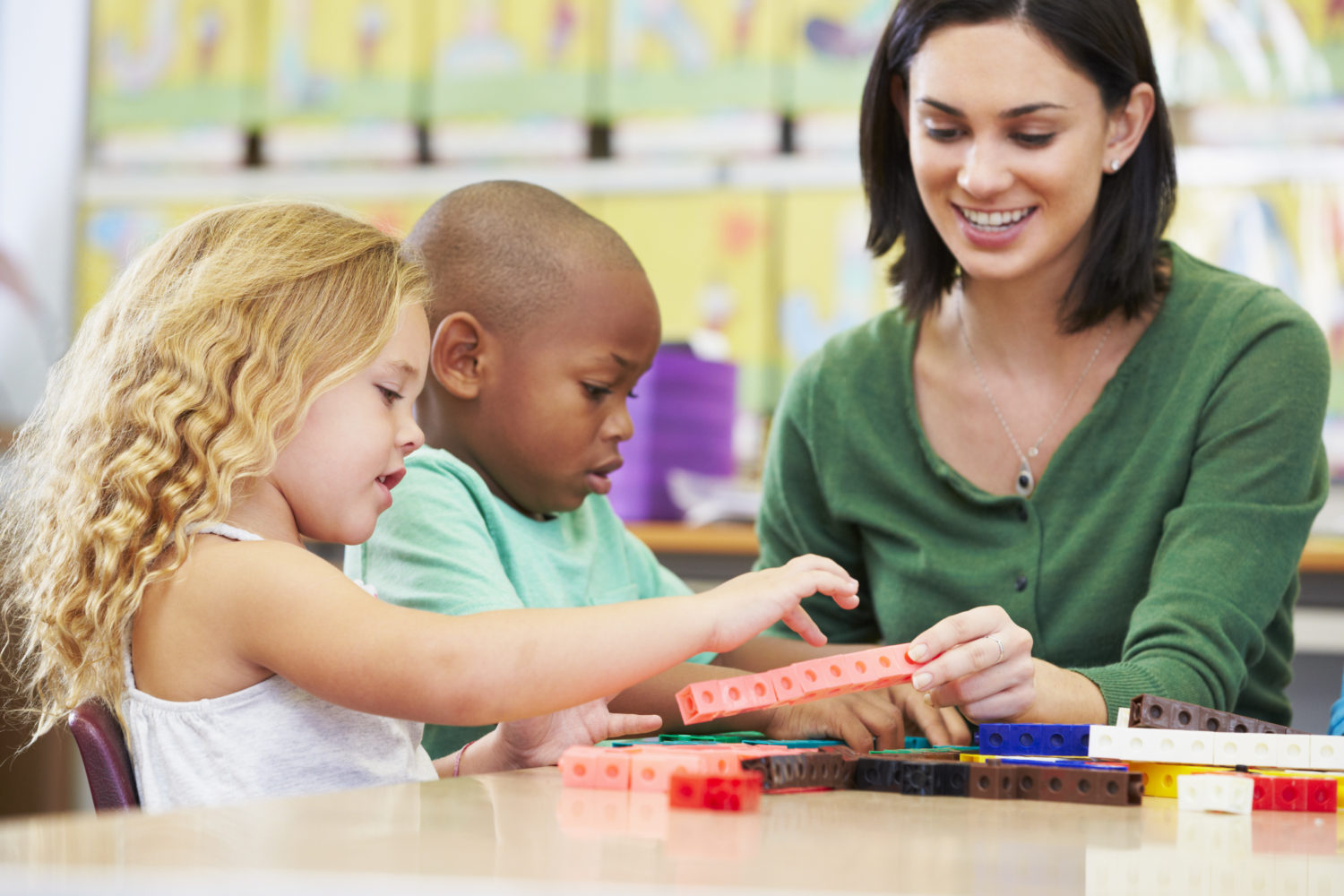 Elementary teacher sitting with two students using manipulative to work on math facts practice.